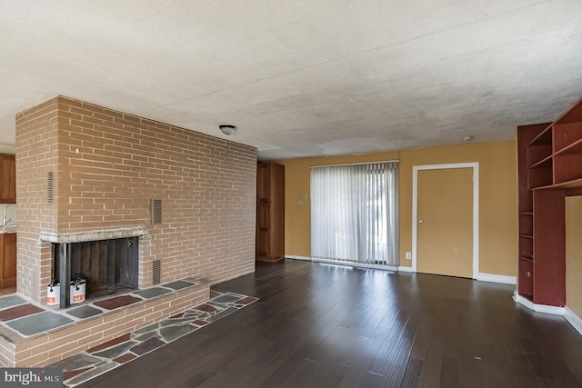 unfurnished living room featuring dark hardwood / wood-style flooring, a textured ceiling, and a brick fireplace