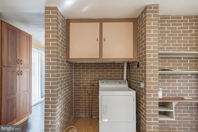 clothes washing area featuring cabinets, dark hardwood / wood-style flooring, washer / dryer, and brick wall