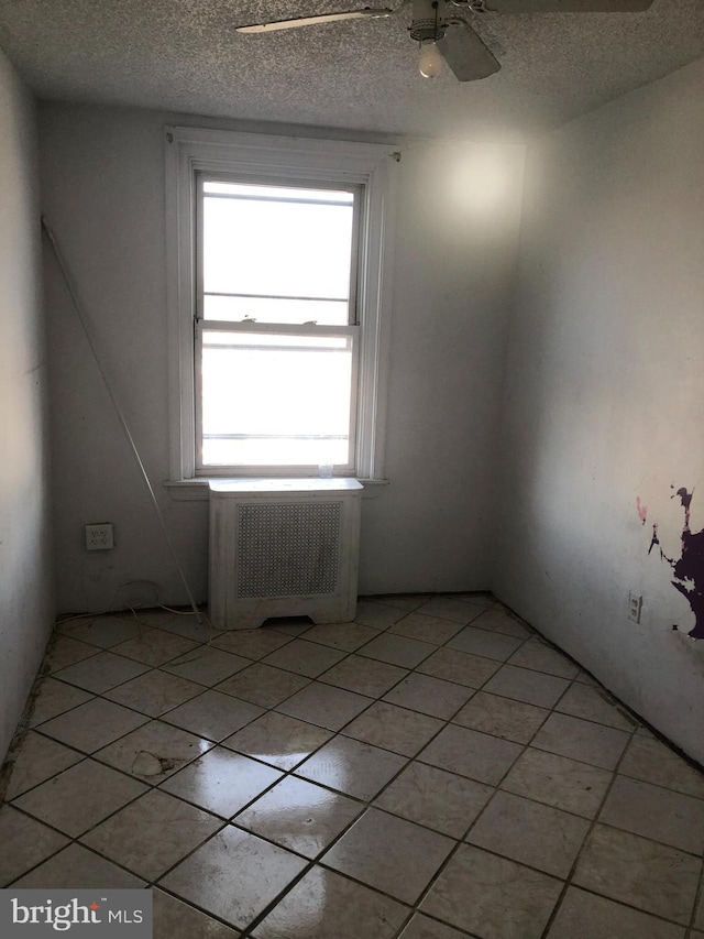 unfurnished room with ceiling fan, a textured ceiling, and radiator heating unit