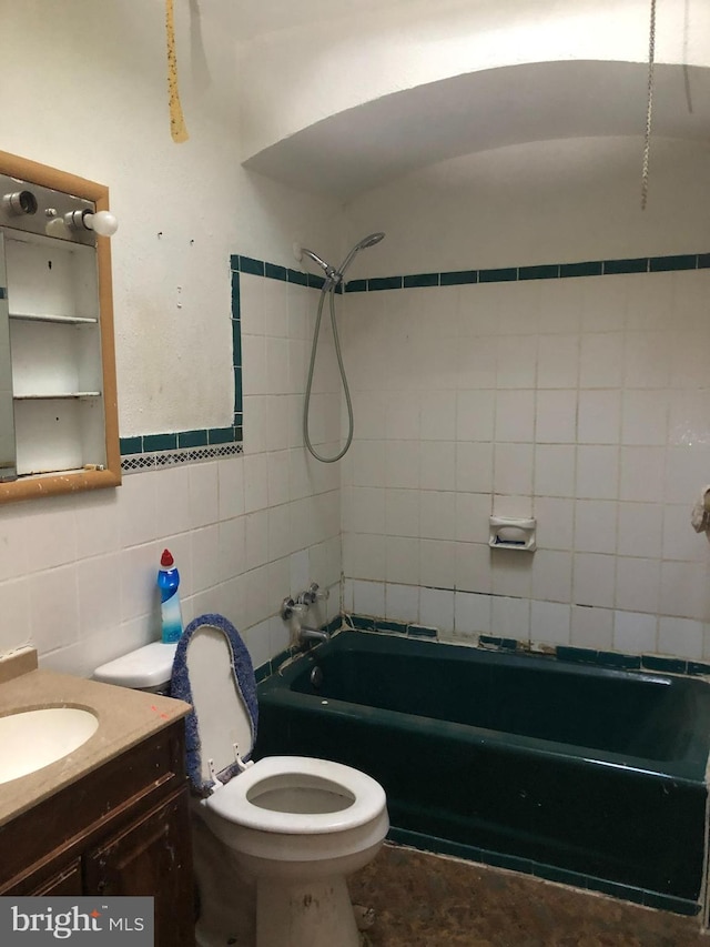 full bathroom with tile walls, tiled shower / bath, toilet, and vanity