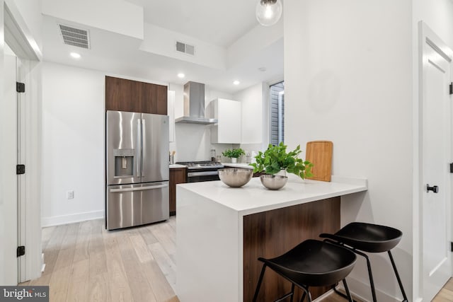 kitchen featuring stainless steel appliances, wall chimney range hood, a kitchen breakfast bar, and light hardwood / wood-style flooring