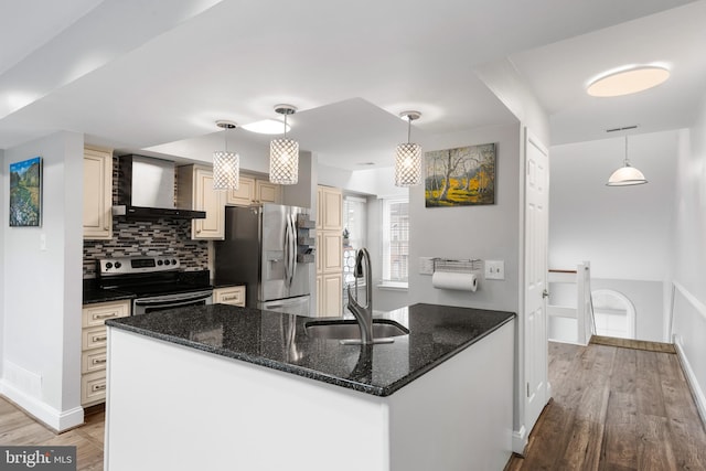 kitchen with sink, hanging light fixtures, wall chimney range hood, dark stone counters, and appliances with stainless steel finishes