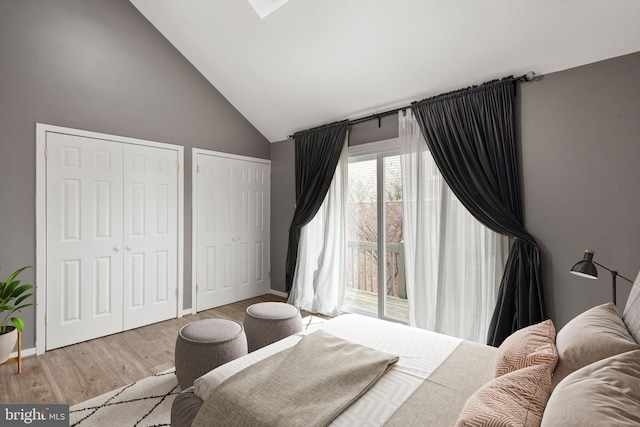 bedroom with multiple closets, high vaulted ceiling, and light hardwood / wood-style flooring