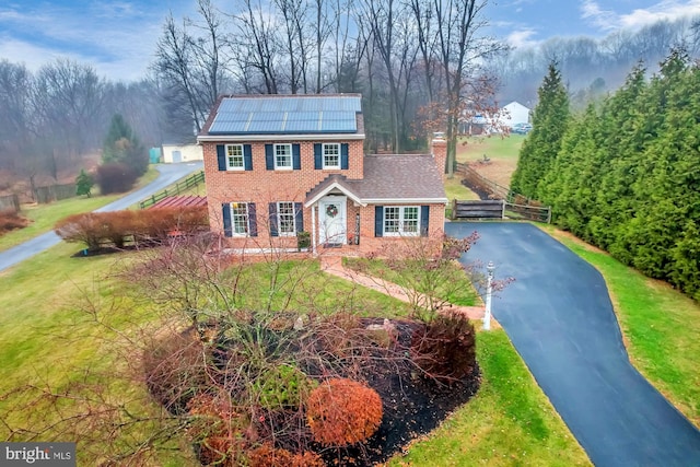 colonial inspired home featuring solar panels and a front lawn