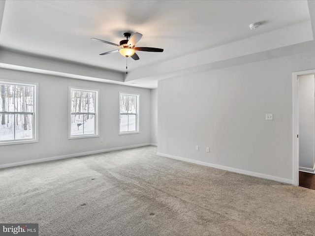 carpeted empty room with a raised ceiling and ceiling fan