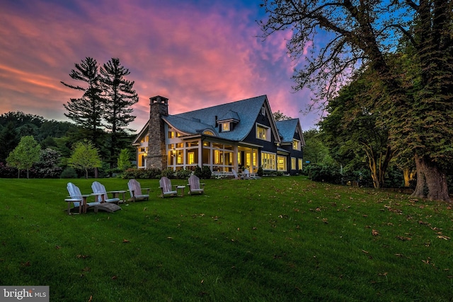 back house at dusk featuring a sunroom and a yard