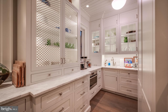 bar featuring light stone countertops, stainless steel oven, sink, white cabinets, and dark hardwood / wood-style floors