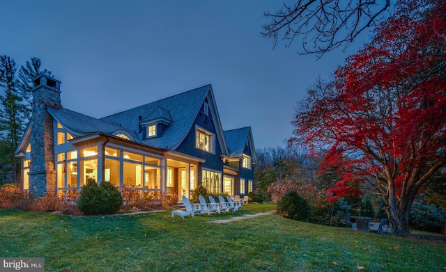 back house at dusk with a sunroom and a yard