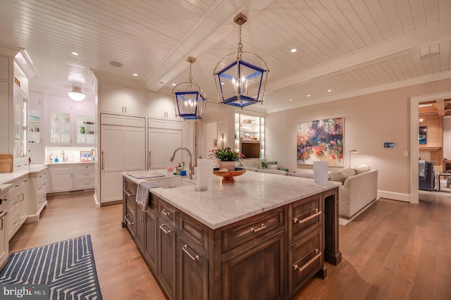 kitchen featuring white cabinetry, light stone counters, pendant lighting, light hardwood / wood-style floors, and a kitchen island with sink