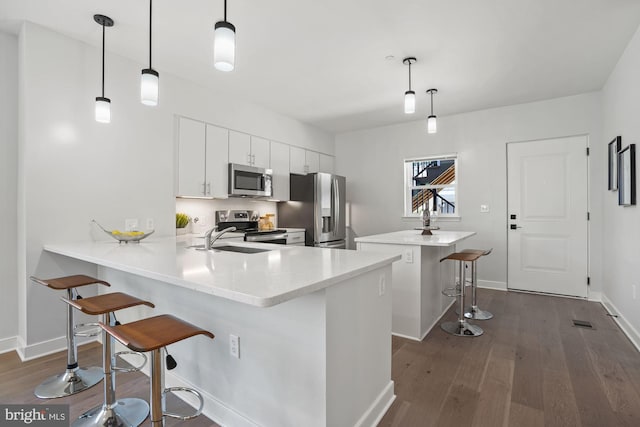 kitchen with kitchen peninsula, decorative light fixtures, white cabinetry, a breakfast bar area, and stainless steel appliances