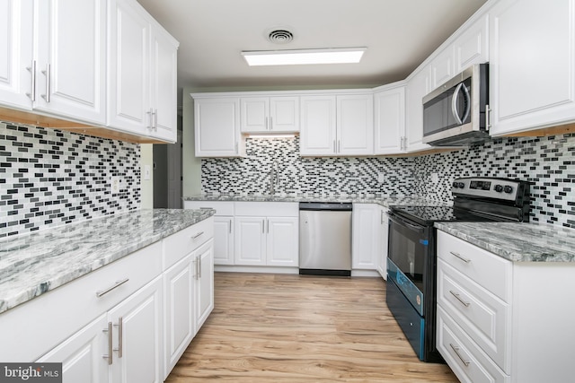 kitchen with backsplash, white cabinets, light wood-type flooring, and stainless steel appliances