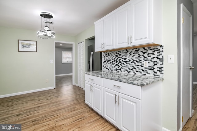 kitchen with white cabinetry, light stone countertops, hanging light fixtures, tasteful backsplash, and light hardwood / wood-style floors