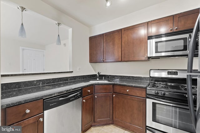 kitchen featuring dark stone counters, stainless steel appliances, sink, light tile patterned floors, and hanging light fixtures