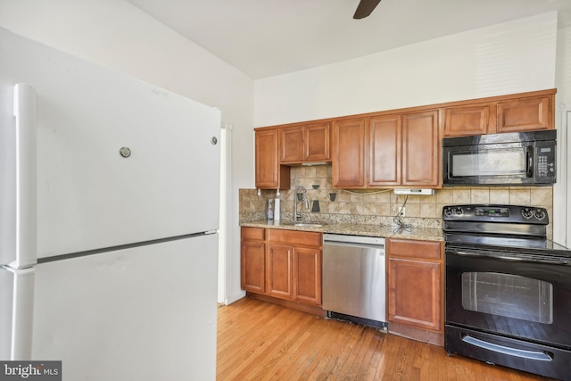 kitchen with light stone counters, decorative backsplash, black appliances, sink, and light wood-type flooring