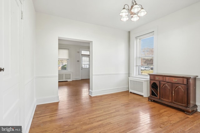 unfurnished living room with radiator, an inviting chandelier, and light wood-type flooring