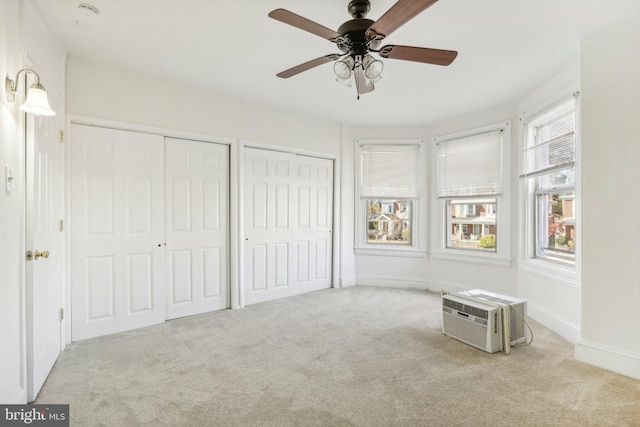 unfurnished bedroom with ceiling fan, light carpet, an AC wall unit, and two closets