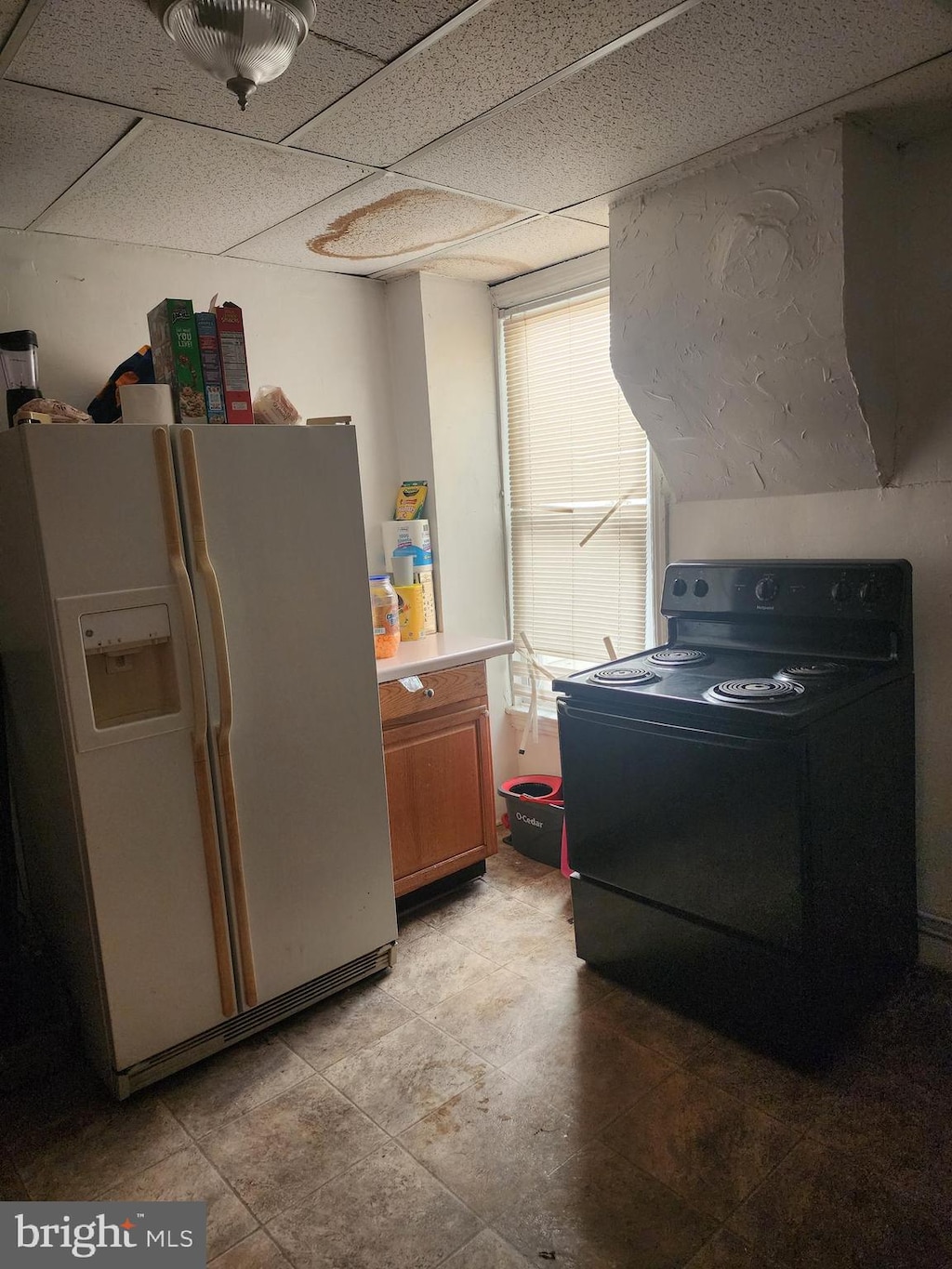 kitchen featuring electric range, a drop ceiling, and white fridge with ice dispenser