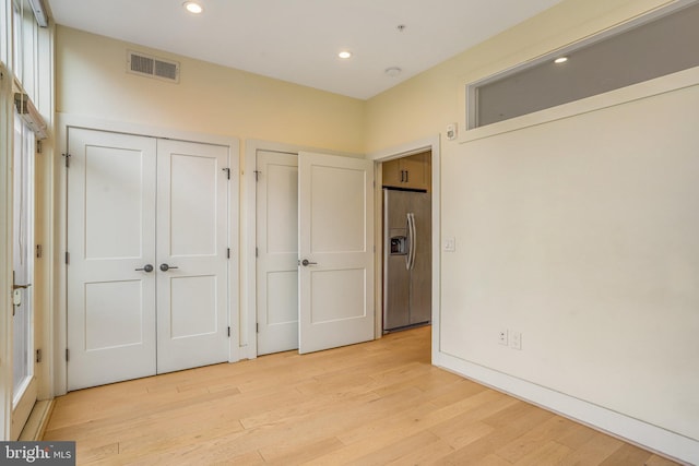 unfurnished bedroom with stainless steel fridge with ice dispenser and light wood-type flooring