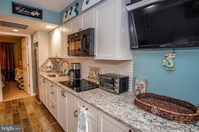 kitchen with sink, tasteful backsplash, light stone counters, white cabinets, and black appliances