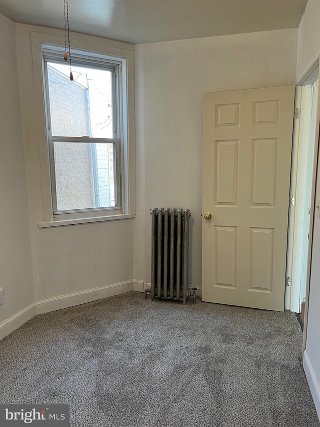 carpeted empty room featuring radiator heating unit