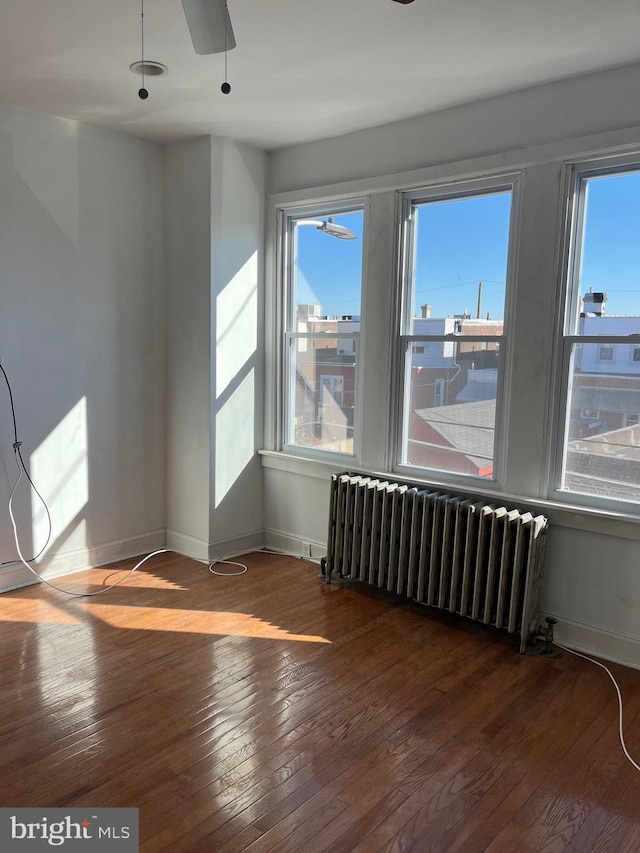 empty room with radiator heating unit, ceiling fan, a wealth of natural light, and wood-type flooring