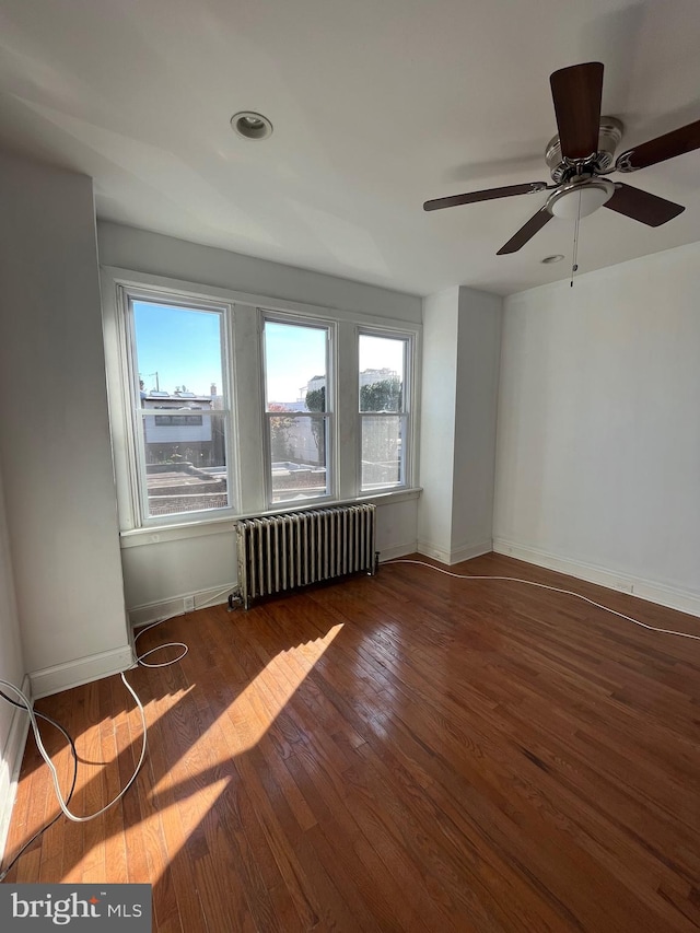 unfurnished room featuring dark hardwood / wood-style floors, ceiling fan, and radiator