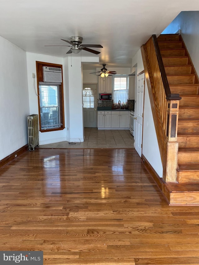 unfurnished living room with ceiling fan, wood-type flooring, radiator, and a wall mounted AC