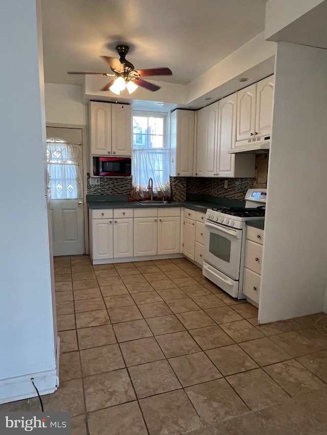 3358 Livingston St, Philadelphia, PA 19134 - kitchen with white range with gas cooktop, under cabinet range hood, light tile patterned flooring, dark countertops, and decorative backsplash