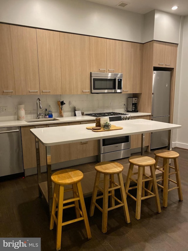 kitchen featuring appliances with stainless steel finishes, dark hardwood / wood-style floors, a kitchen breakfast bar, and sink