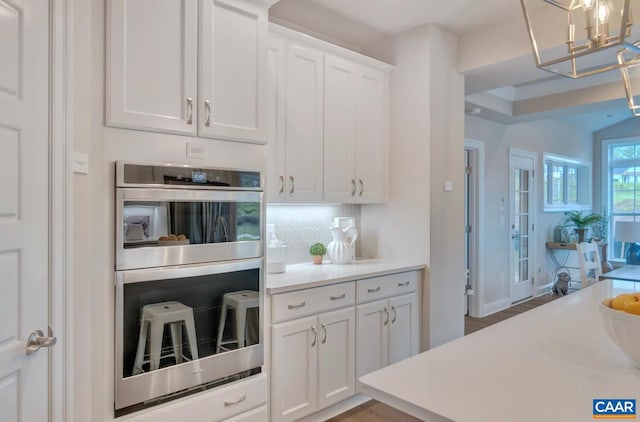 kitchen with decorative backsplash, dark wood-type flooring, white cabinets, and stainless steel double oven