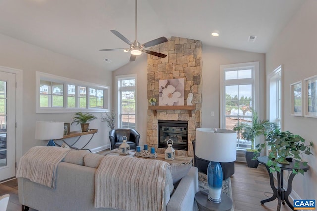 living room featuring hardwood / wood-style flooring, ceiling fan, a stone fireplace, and vaulted ceiling