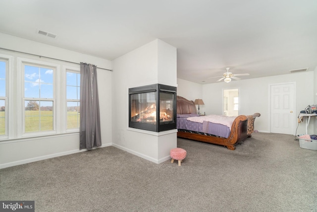 carpeted bedroom featuring a multi sided fireplace and ceiling fan