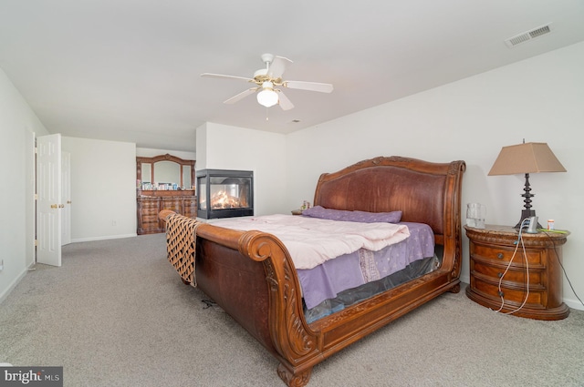 carpeted bedroom with ceiling fan and a multi sided fireplace