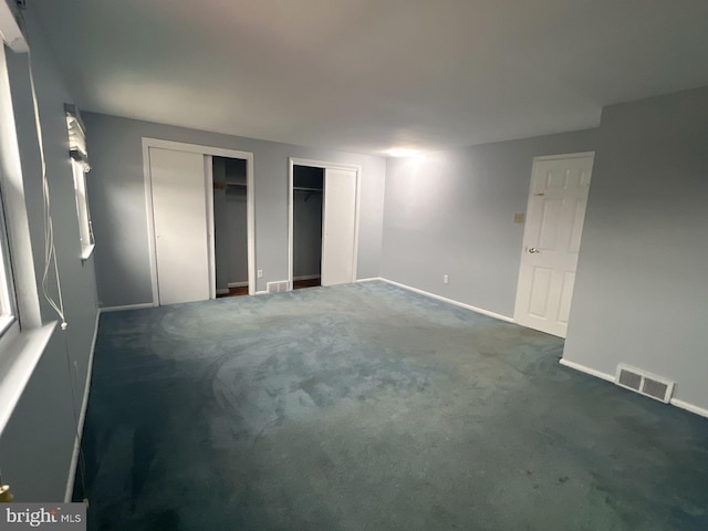 unfurnished bedroom with multiple closets and dark carpet