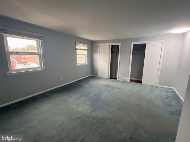 unfurnished bedroom with dark colored carpet, multiple windows, and two closets