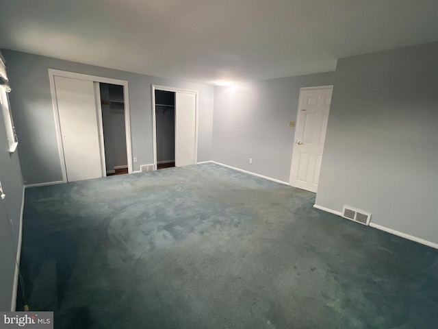 unfurnished bedroom featuring multiple closets and dark carpet