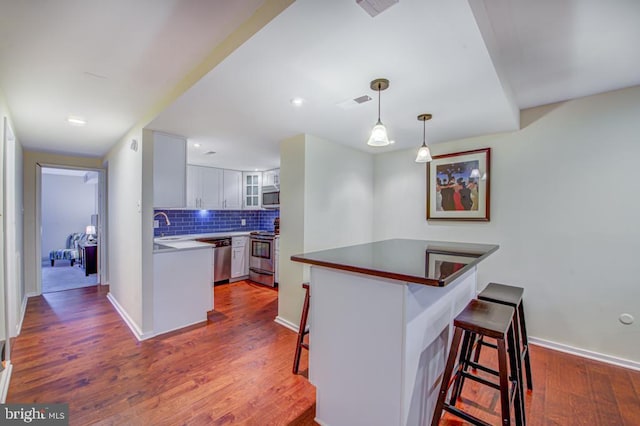 kitchen featuring white cabinetry, kitchen peninsula, hardwood / wood-style floors, a breakfast bar area, and appliances with stainless steel finishes