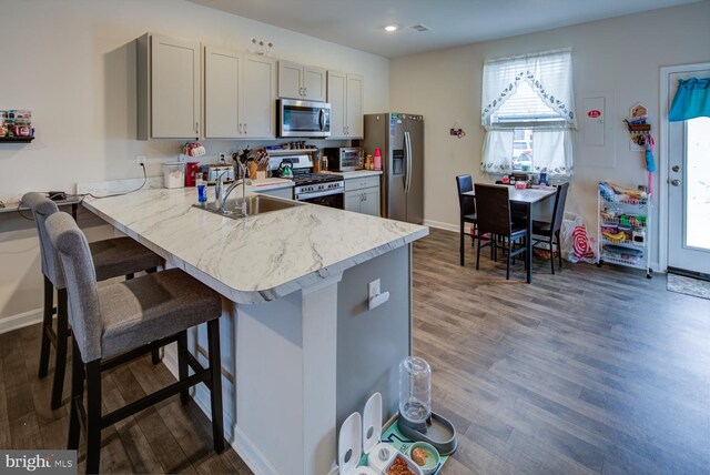 kitchen featuring kitchen peninsula, a breakfast bar, stainless steel appliances, gray cabinets, and dark hardwood / wood-style floors