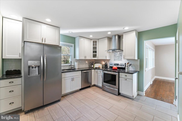 kitchen featuring sink, stainless steel appliances, white cabinetry, and wall chimney range hood