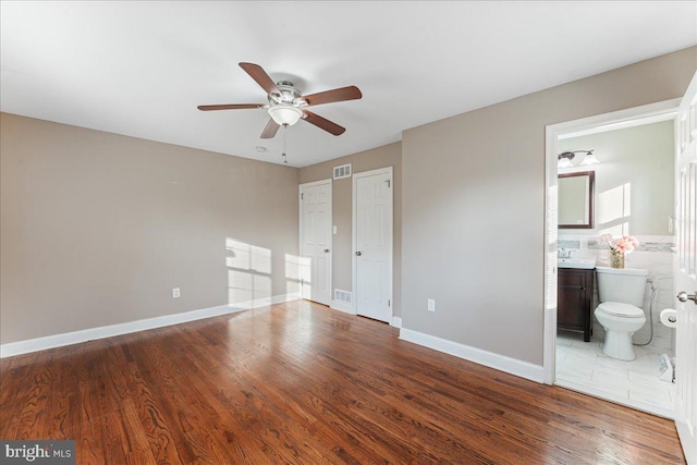 unfurnished bedroom featuring ensuite bath, ceiling fan, and hardwood / wood-style flooring