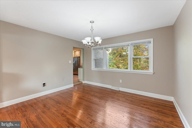 spare room featuring hardwood / wood-style floors and a notable chandelier