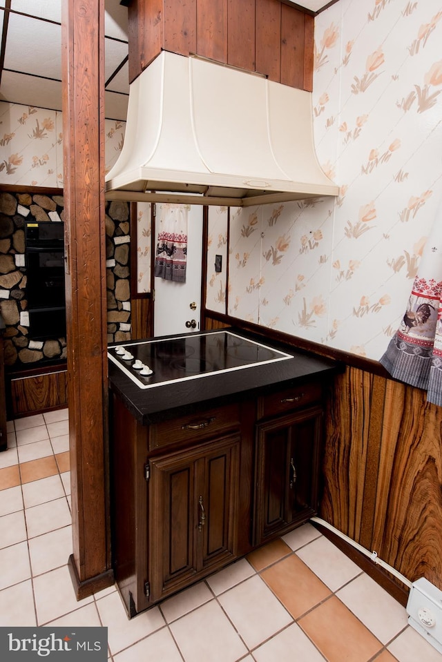 kitchen with dark brown cabinetry, exhaust hood, light tile patterned floors, and black electric stovetop