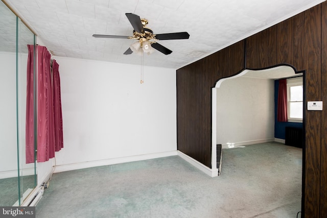 empty room featuring radiator, carpet, wooden walls, and ceiling fan