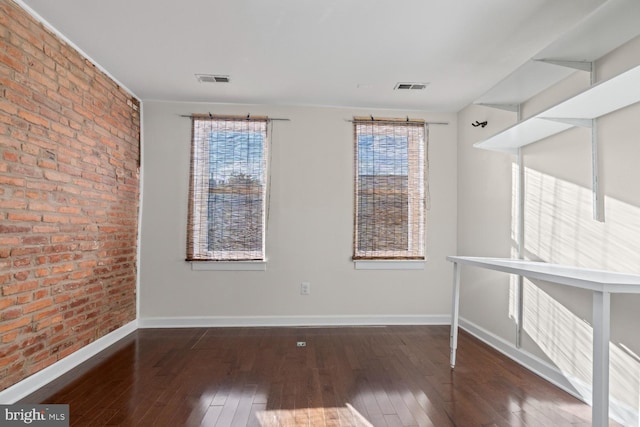 unfurnished room with dark hardwood / wood-style flooring and brick wall