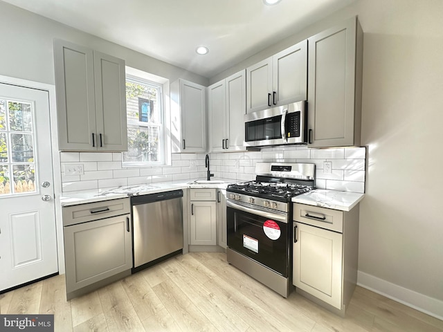 kitchen with gray cabinetry, light stone counters, stainless steel appliances, backsplash, and light hardwood / wood-style floors