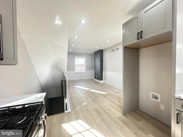 kitchen with gray cabinets, stainless steel range with gas stovetop, light stone counters, and light hardwood / wood-style floors