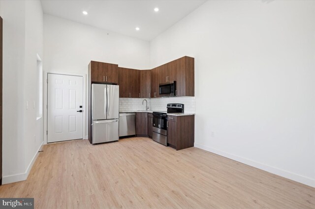 kitchen with sink, backsplash, light wood-type flooring, appliances with stainless steel finishes, and a high ceiling