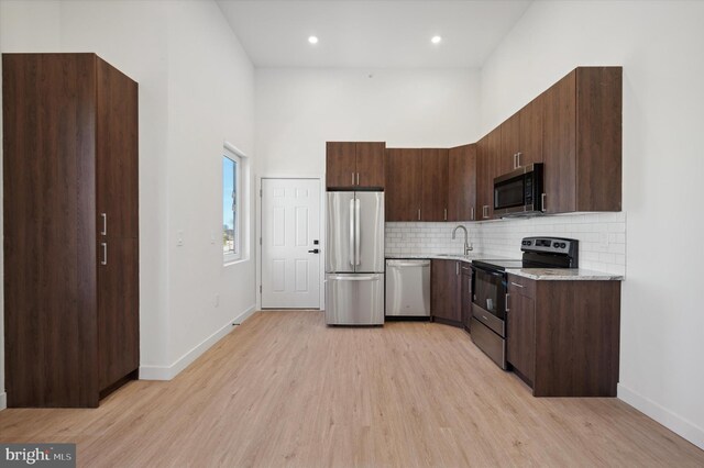 kitchen with stainless steel appliances, light wood-type flooring, dark brown cabinets, light stone countertops, and sink