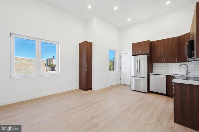 kitchen with stainless steel appliances, light hardwood / wood-style floors, a healthy amount of sunlight, and a towering ceiling