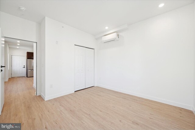 unfurnished bedroom featuring a wall mounted AC, light wood-type flooring, a closet, and stainless steel fridge